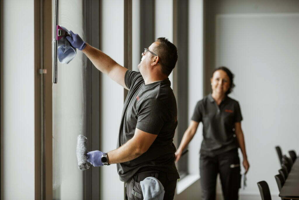 To Ability-medarbeidere vasker vinduer innenfra