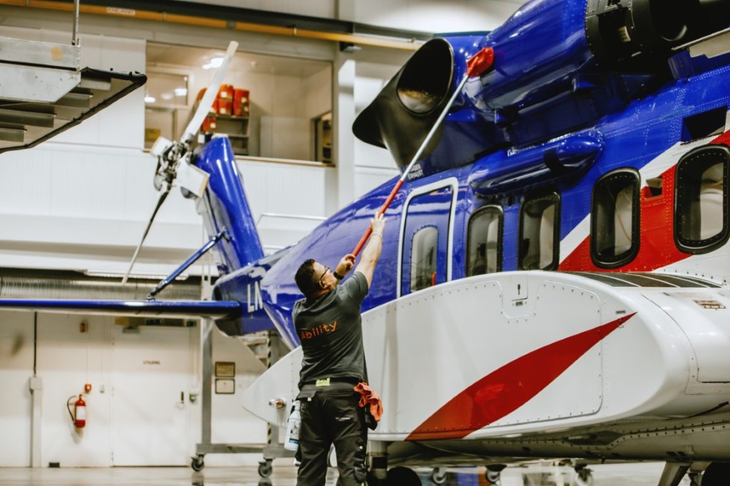 En renholder vasker et helikopter i en hangar.