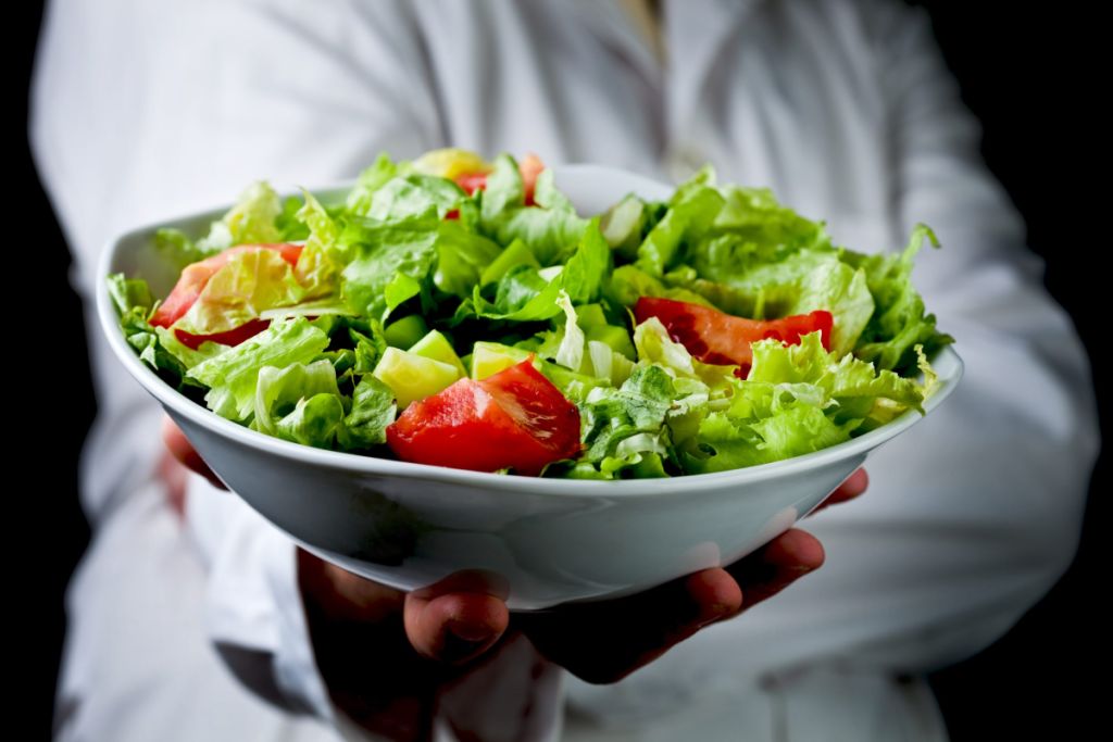 En kokk holder fram en skål med frisk grønn salat