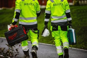 To arbeidere i arbeidsantrekk med Ability på ryggen bærer utstyr og hjelm Ability FM Ability FM