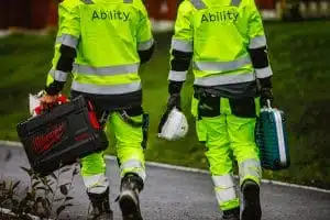 To arbeidere i arbeidsantrekk (med Ability på ryggen) bærer utstyr og hjelm